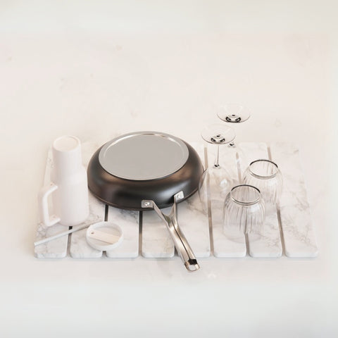Stone dish drying mat on kitchen counter with frying pan, wine glasses, tumbler, and other dishes on top