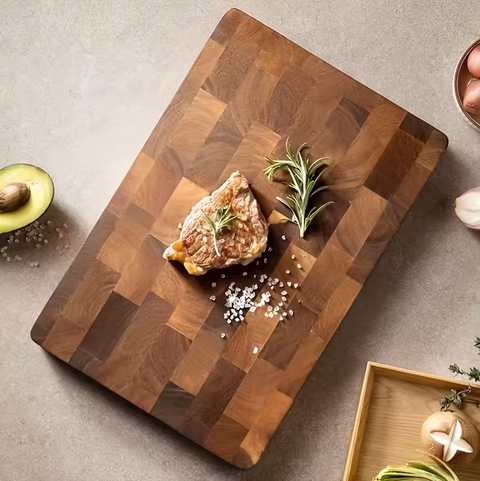 Wooden cutting board with a piece of meat, rosemary, and salt on a gray surface.